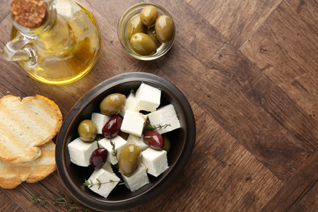 Marinated olives with feta cheese, bread pieces, butter and rosemary on wooden table, flat lay. Space for textの写真素材