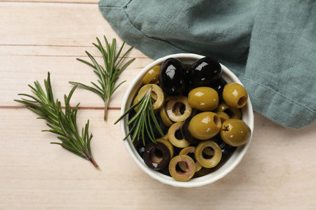 Different delicious marinated olive rings, whole ones and rosemary in bowl on light wooden table, flat layの写真素材