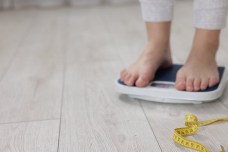 Woman on scales and measuring tape on floor indoors, selective focus with space for text. Weight...