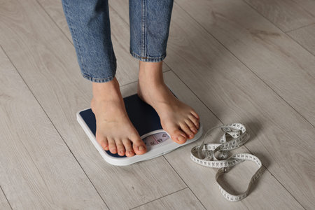 Woman on scales and measuring tape indoors, closeup.