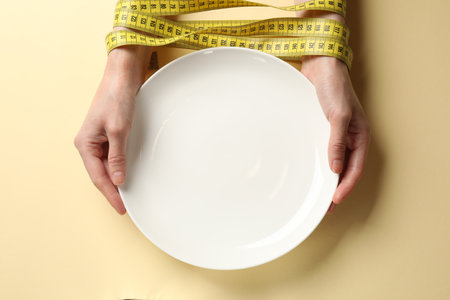 Woman tied with measuring tape and plate on beige background, top viewの写真素材