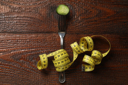 Fork with slice of cucumber and measuring tape on wooden table, flat layの写真素材