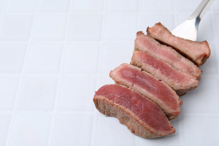 Delicious sliced beef tenderloin with different degrees of doneness on light tiled table, closeup. Space for textの写真素材