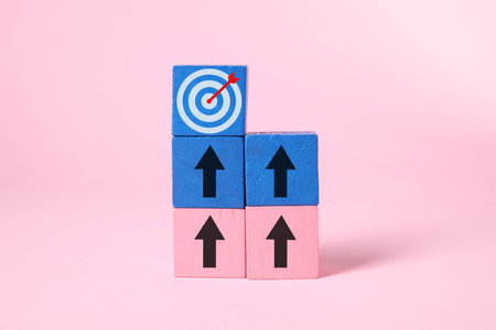 Targeting. Stacked cubes with arrows pointing at one with bullseye on top against pink backgroundの写真素材