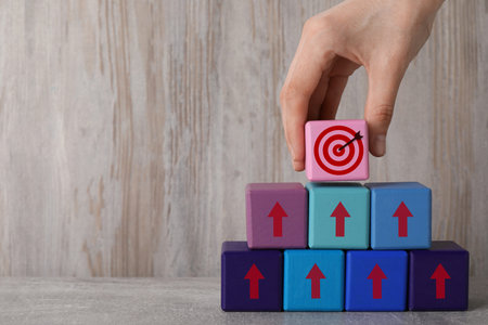 Targeting. Woman putting cube with bullseye on top of pyramid of other ones with arrows on wooden...