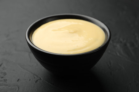 Tasty cheese sauce in bowl on black table, closeupの写真素材