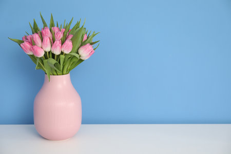 Bouquet of beautiful tulips in vase on white table against light blue background, space for textの写真素材
