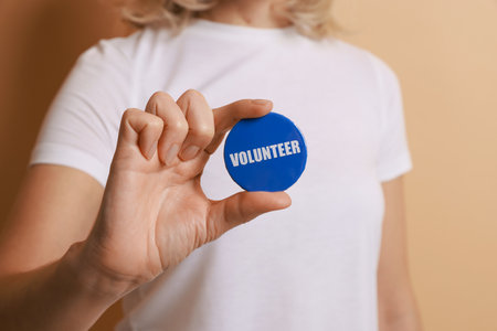 Woman holding button badge with word Volunteer on beige background, closeupの写真素材