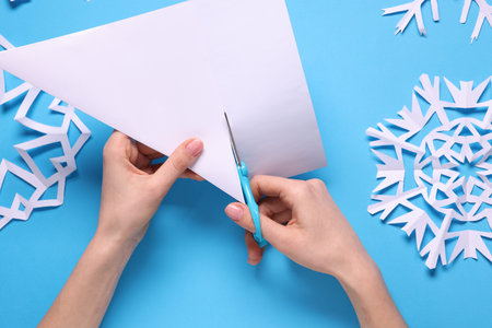 Woman making paper snowflake on light blue background, top viewの写真素材