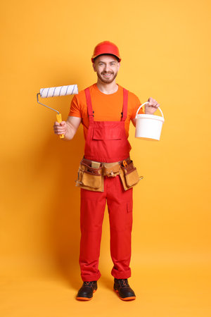 Professional painter with roller and bucket of paint on orange backgroundの写真素材