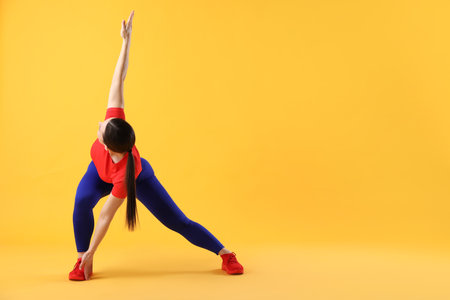 Woman in sportswear exercising on orange backgroundの写真素材