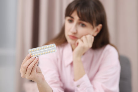 Upset woman with blister of contraceptive pills indoors, selective focusの写真素材