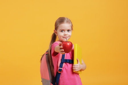 Cute little girl with book and apple on orange backgroundの写真素材