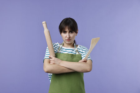 Woman with rolling pin and turner on violet backgroundの写真素材