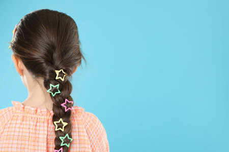 Little girl wearing beautiful hair accessories on light blue background, back view. Space for text
