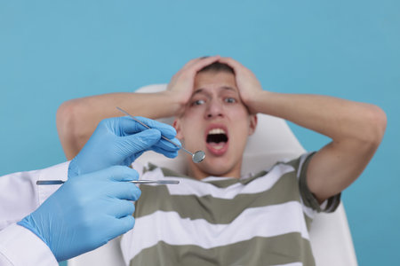 Scared man having appointment with dentist on light blue background, selective focusの写真素材