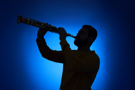 Professional musician playing soprano saxophone on blue background, backlitの写真素材