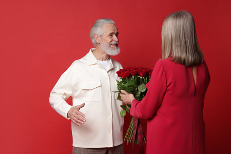 Man presenting bouquet of roses to his wife on red backgroundの写真素材