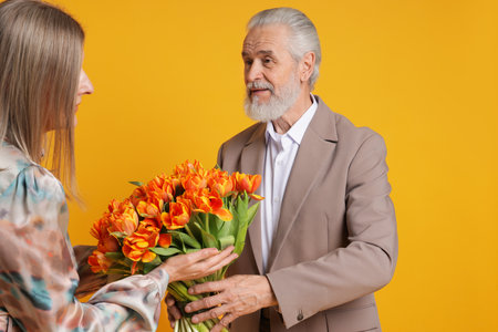 Man presenting bouquet of tulips to his wife on yellow backgroundの写真素材