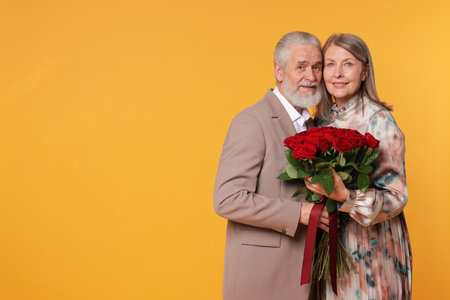 Happy couple with bouquet of red roses on yellow background. Space for textの写真素材