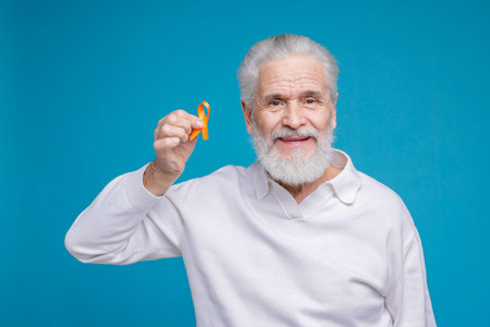 Multiple Sclerosis awareness. Senior man with orange ribbon on light blue background