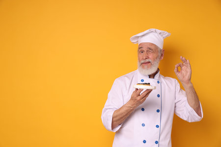 Professional pastry chef with tart showing ok gesture on orange background, space for textの写真素材