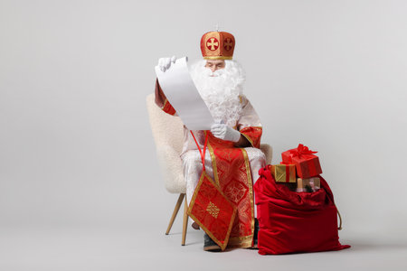 Saint Nicholas with wish list and sack full of gifts on light grey backgroundの写真素材