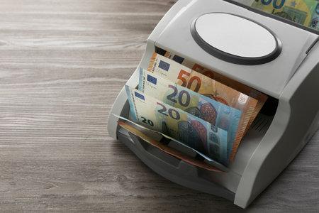 Money counter machine with euro banknotes on wooden table, closeup. Space for textの写真素材