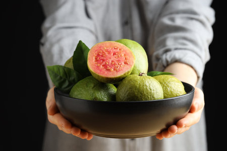 Woman with bowl of fresh guava fruits on black background, closeupの写真素材