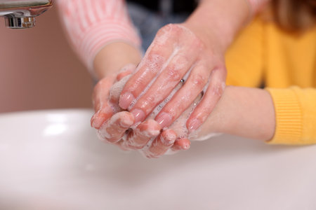 Mother and daughter washing their hands above sink indoors, closeupの写真素材