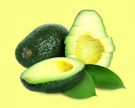 Whole and cut avocado fruits and green leaves on yellow backgroundの写真素材