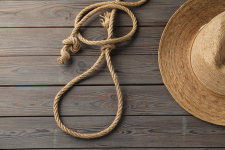 Lasso made of cotton rope and straw hat on wooden background, flat lay