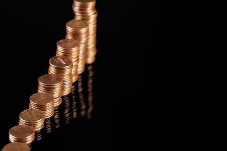Stacks of coins on black mirror surface, closeup. Space for text