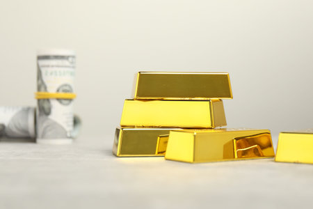 Shiny gold bars and dollar banknotes on light table against grey background, selective focusの写真素材