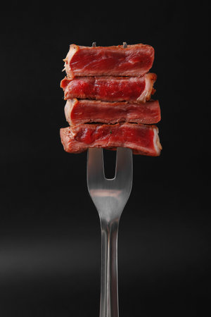 Carving fork with pieces of delicious beef meat on black background, closeupの写真素材
