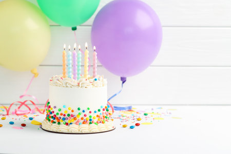 Delicious cake with colorful sprinkles and burning candles on white table. Space for textの写真素材