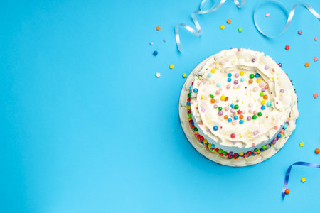Delicious cake with colorful sprinkles and streamers on light blue background, flat lay. Space for textの写真素材