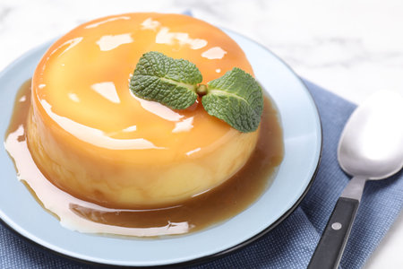 Delicious pudding with caramel sauce and mint on white table, closeup