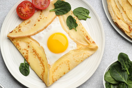 Delicious crepes with egg, tomato and basil on light grey table, flat layの写真素材