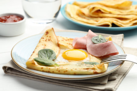 Delicious crepes with egg, ham, basil and sauce on white wooden table, closeupの写真素材