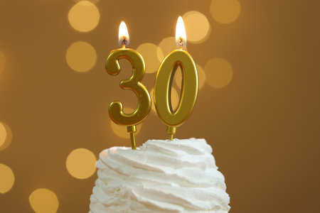 30th birthday. Burning number shaped candles on cupcake against golden background with blurred lights, closeup. Bokeh effectの写真素材