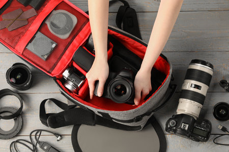 Photographer with professional equipment and backpack at light wooden table, top view