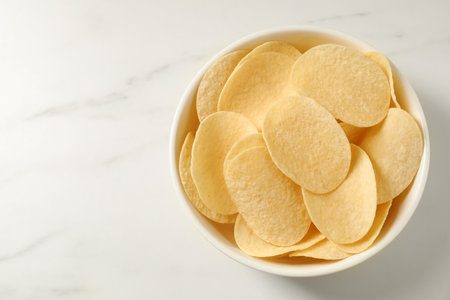 Tasty potato chips in bowl on white marble table, top view. Space for textの写真素材