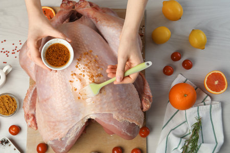 Woman applying marinade onto raw turkey at white wooden table, top viewの写真素材