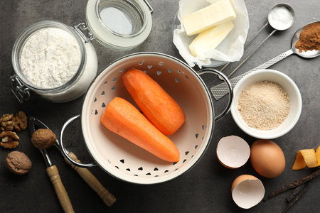 Different ingredients for making carrot cake and kitchenware on dark textured table, flat layの写真素材