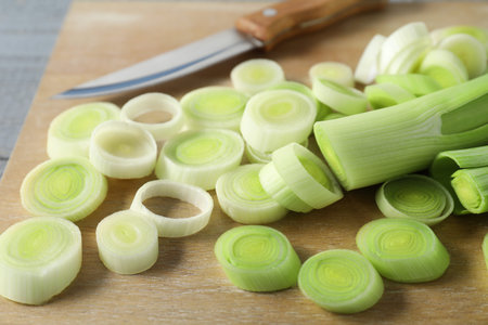 Fresh chopped leeks and knife on wooden table, closeup