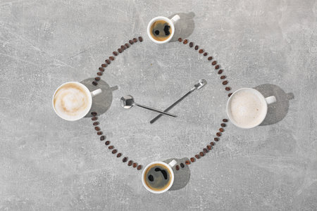 Cups of coffee, beans and spoons representing clock on grey table, flat lay