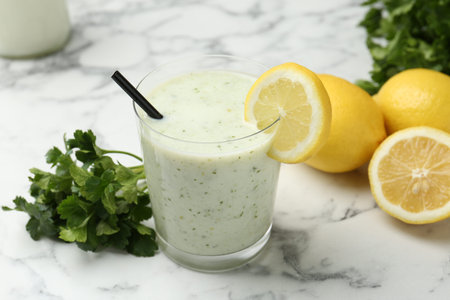 Healthy parsley drink in glass, leaves and lemons on white marble table, closeupの写真素材