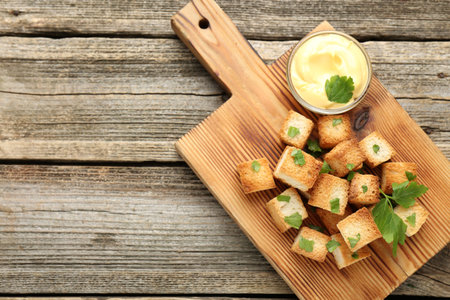 Tasty crispy croutons with cut parsley and sauce on wooden table, top view. Space for textの写真素材