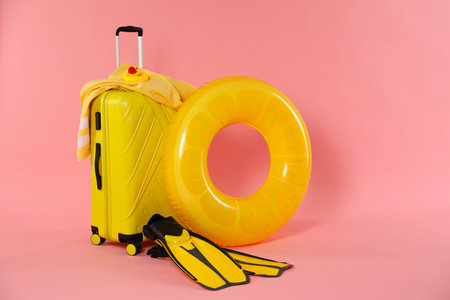 Yellow inflatable ring, flippers, suitcase, beach towel and toy on pink background, space for textの写真素材